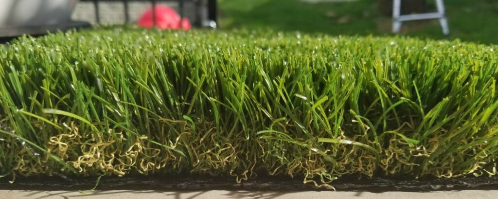 Detailed close-up of artificial grass turf pile, showing green blades, yellow thatch layer, and black backing.